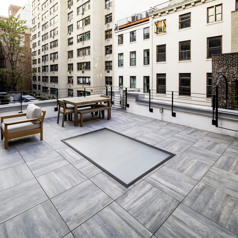 A rooftop patio with seating and a large glass floor panel overlooking city buildings.