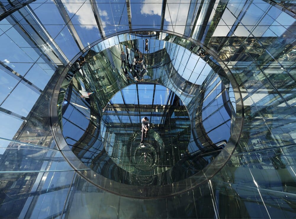 Circular glass observation deck reflecting people and panoramic views.