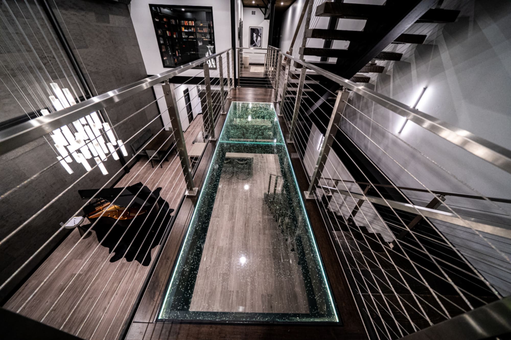 A long illuminated glass walkway suspended between two modern architectural structures in a monochrome interior.