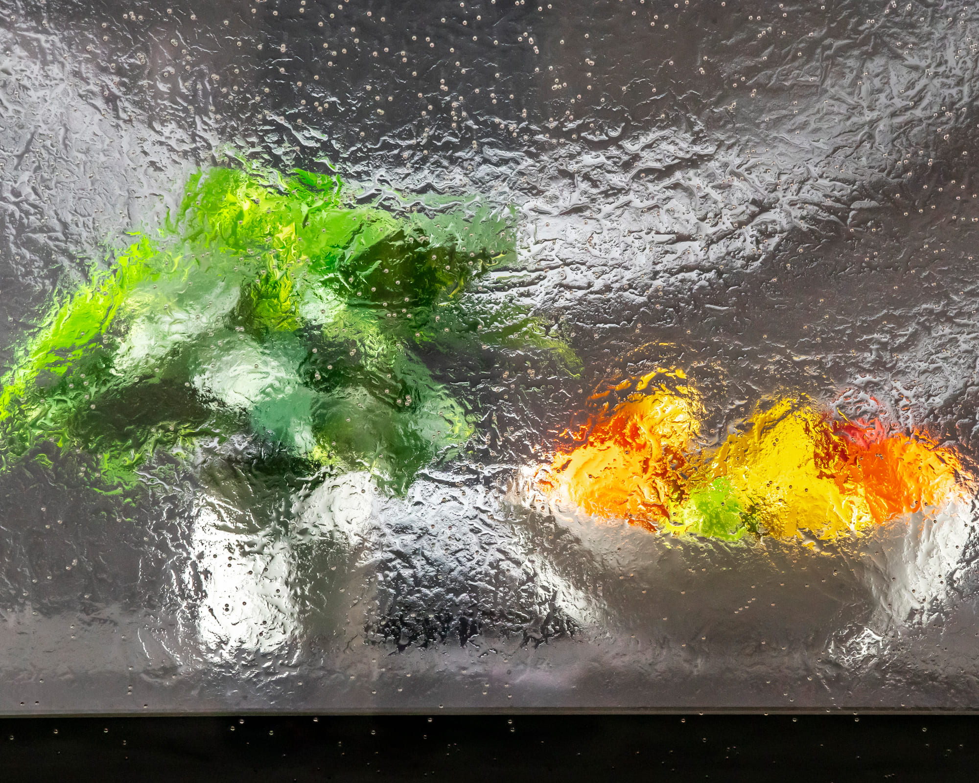 A textured, abstract glass surface with bright green, yellow, and orange fruits beneath