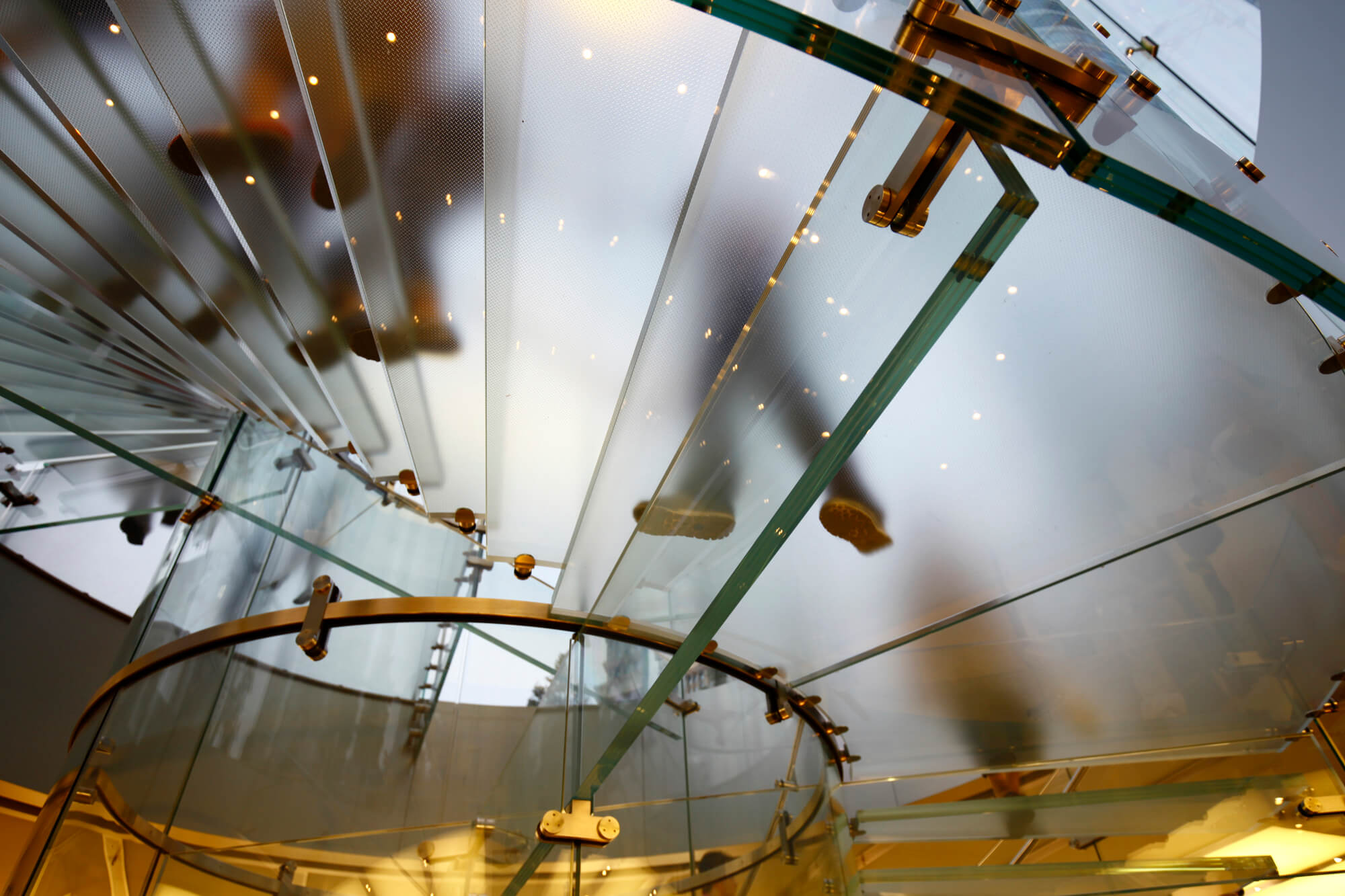 Upward view of a curved glass ceiling with metal framing and suspended architectural elements.