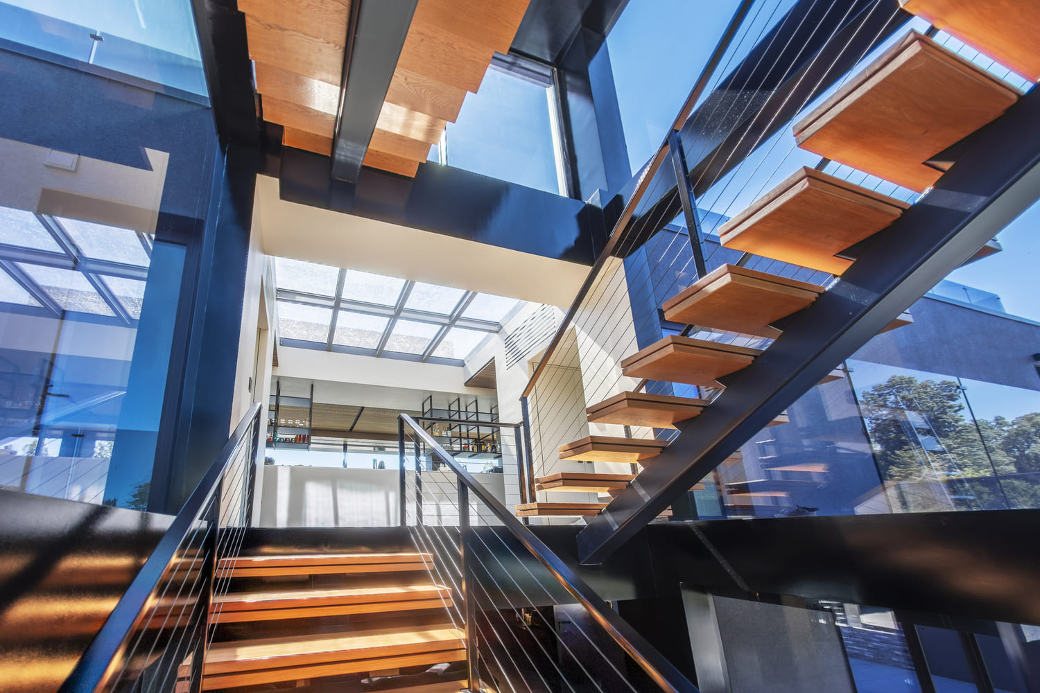 Modern staircase illuminated by a large architectural skylight framed with steel and wood accents.