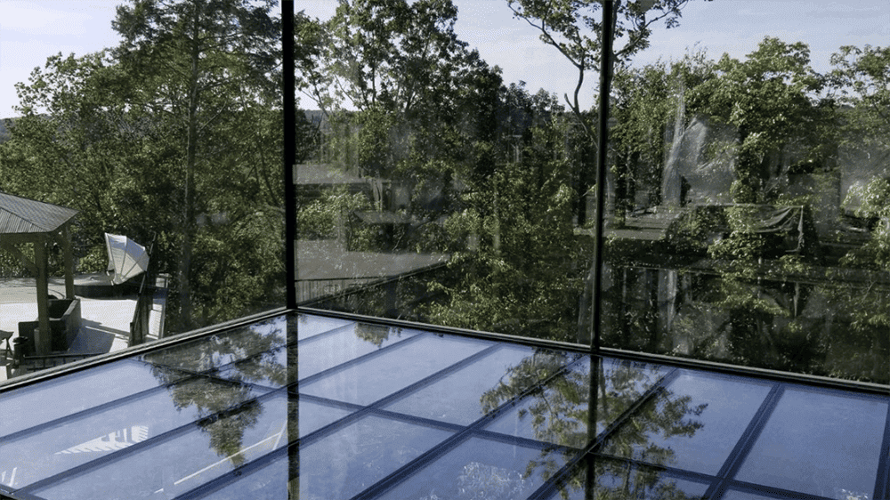 Modern home with floor-to-ceiling glass walls reflecting surrounding trees and landscape.