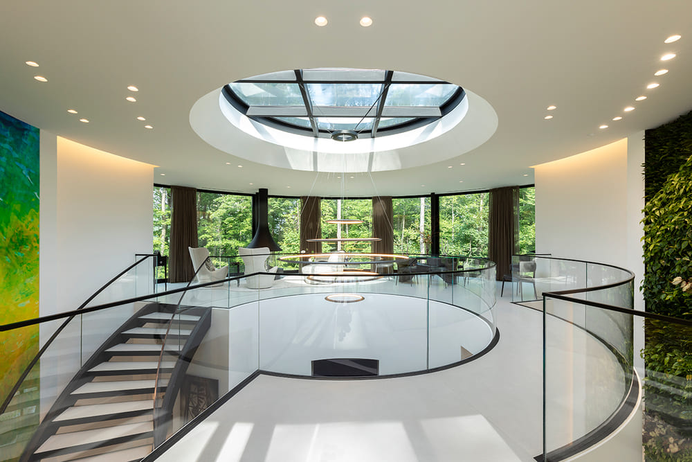 Circular skylight above a modern hallway leading to a sleek interior staircase with glass railings.