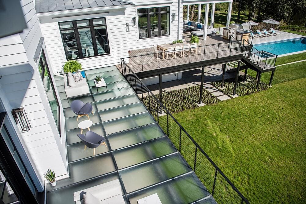 Backyard with an elevated glass deck overlooking a lawn, adjacent to a contemporary white home.