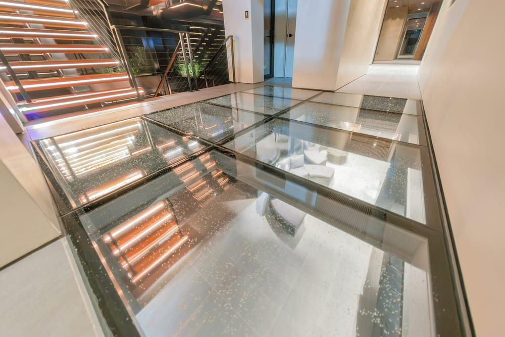 Glass floor section installed over a lower-level space with wooden ceiling slats reflecting on the surface.