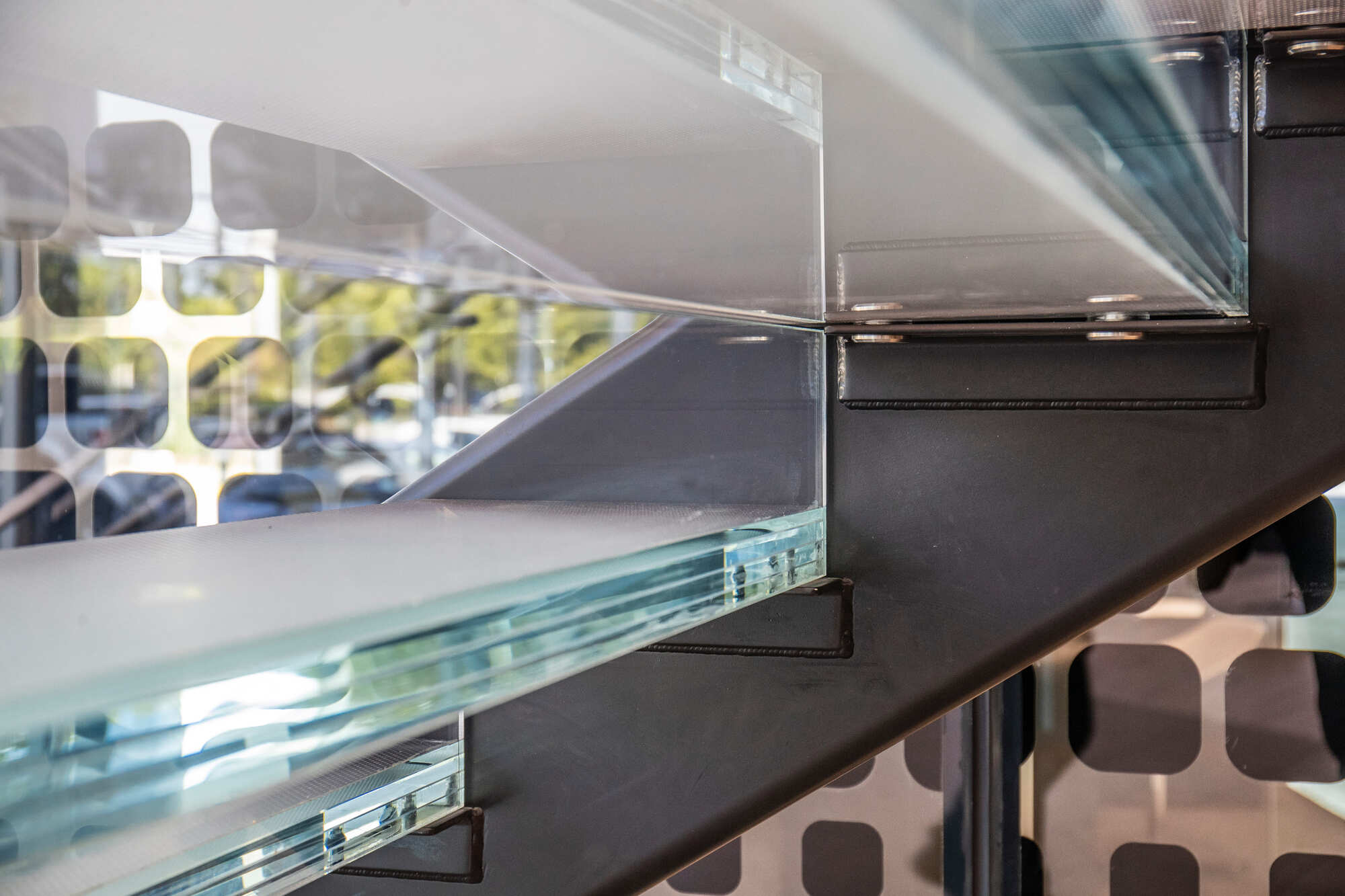 Close-up of thick glass stair treads embedded into a sleek black metal staircase structure.