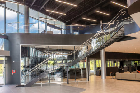 A glass staircase is illuminated by natural light, highlighting the clarity and layered edges of the laminated glass steps in a commercial setting.