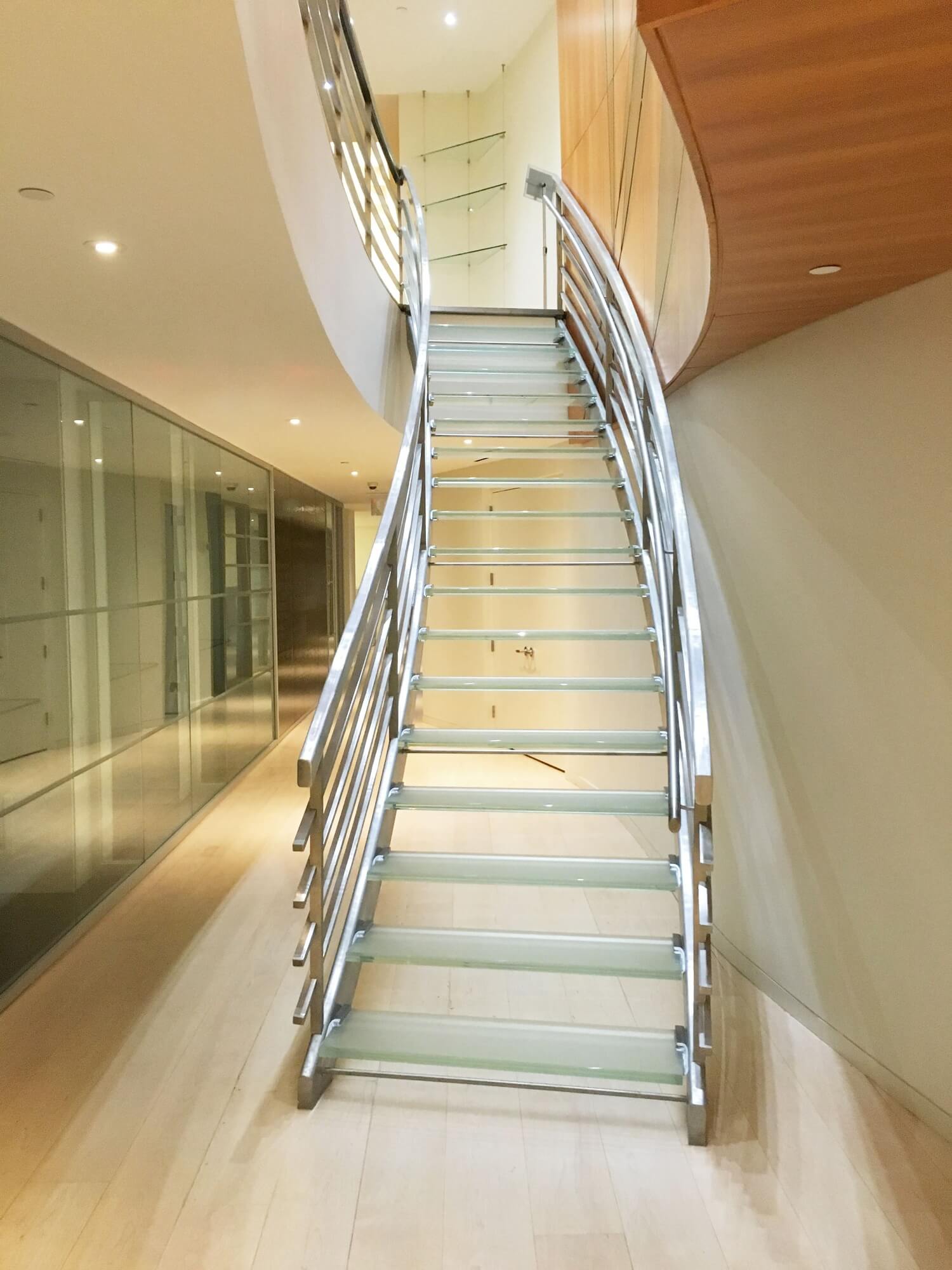 Curved glass staircase with stainless steel railings and soft overhead lighting.