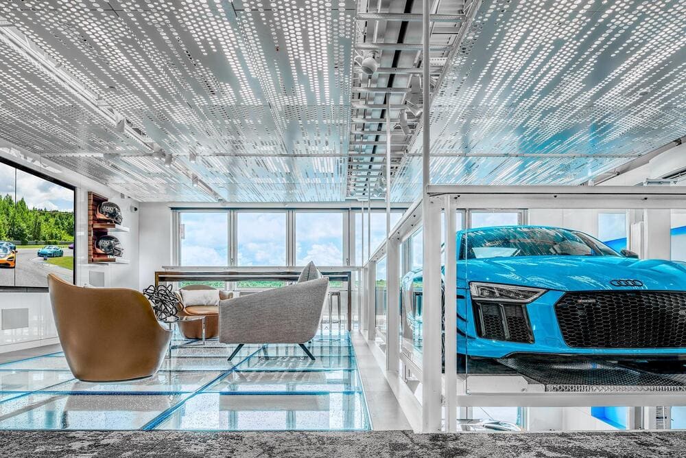 Bright interior space with large glass walls revealing an automotive showroom outside.