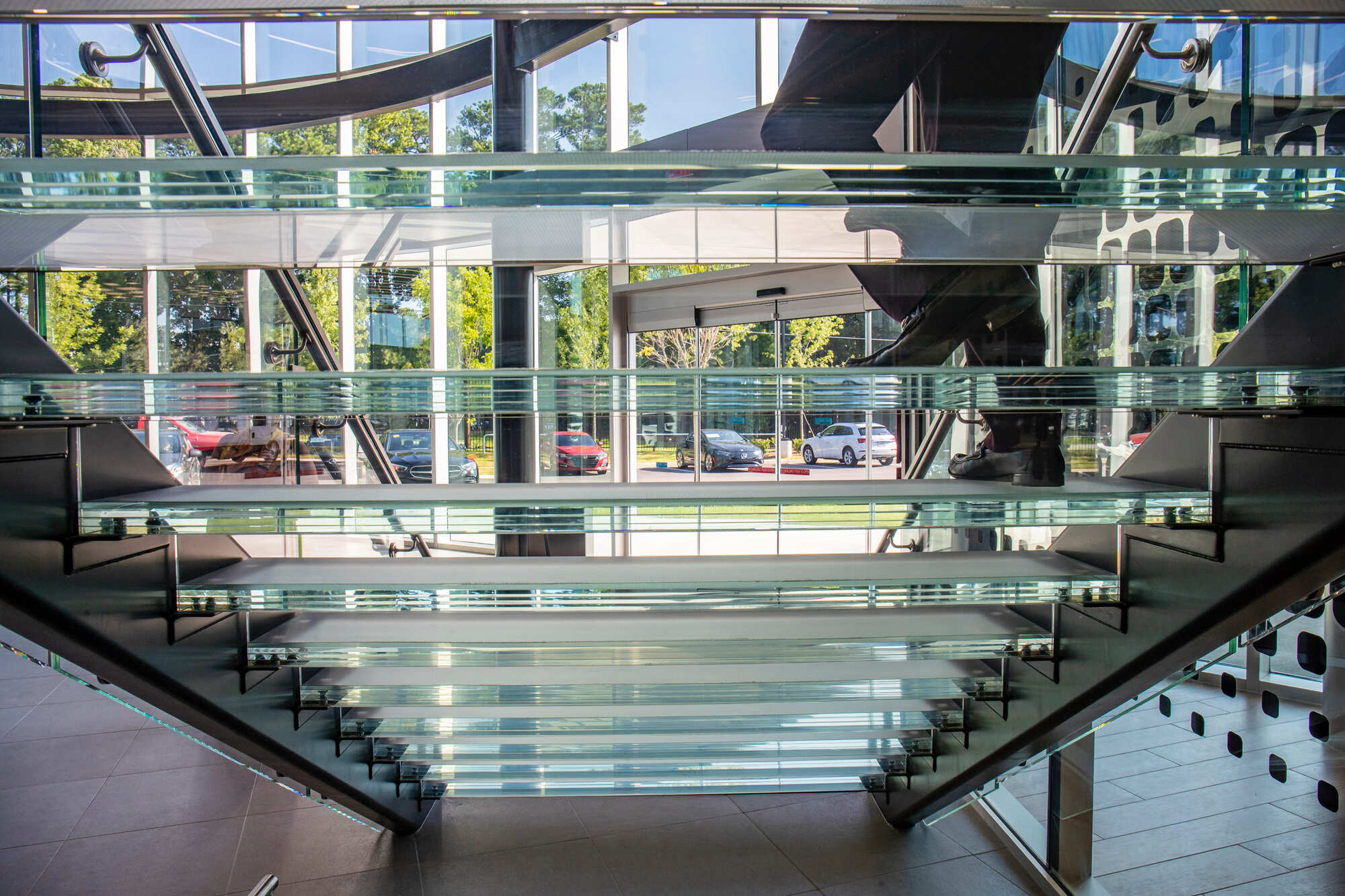 Bottom view of a glass staircase showing transparent treads and glass railings with natural light.