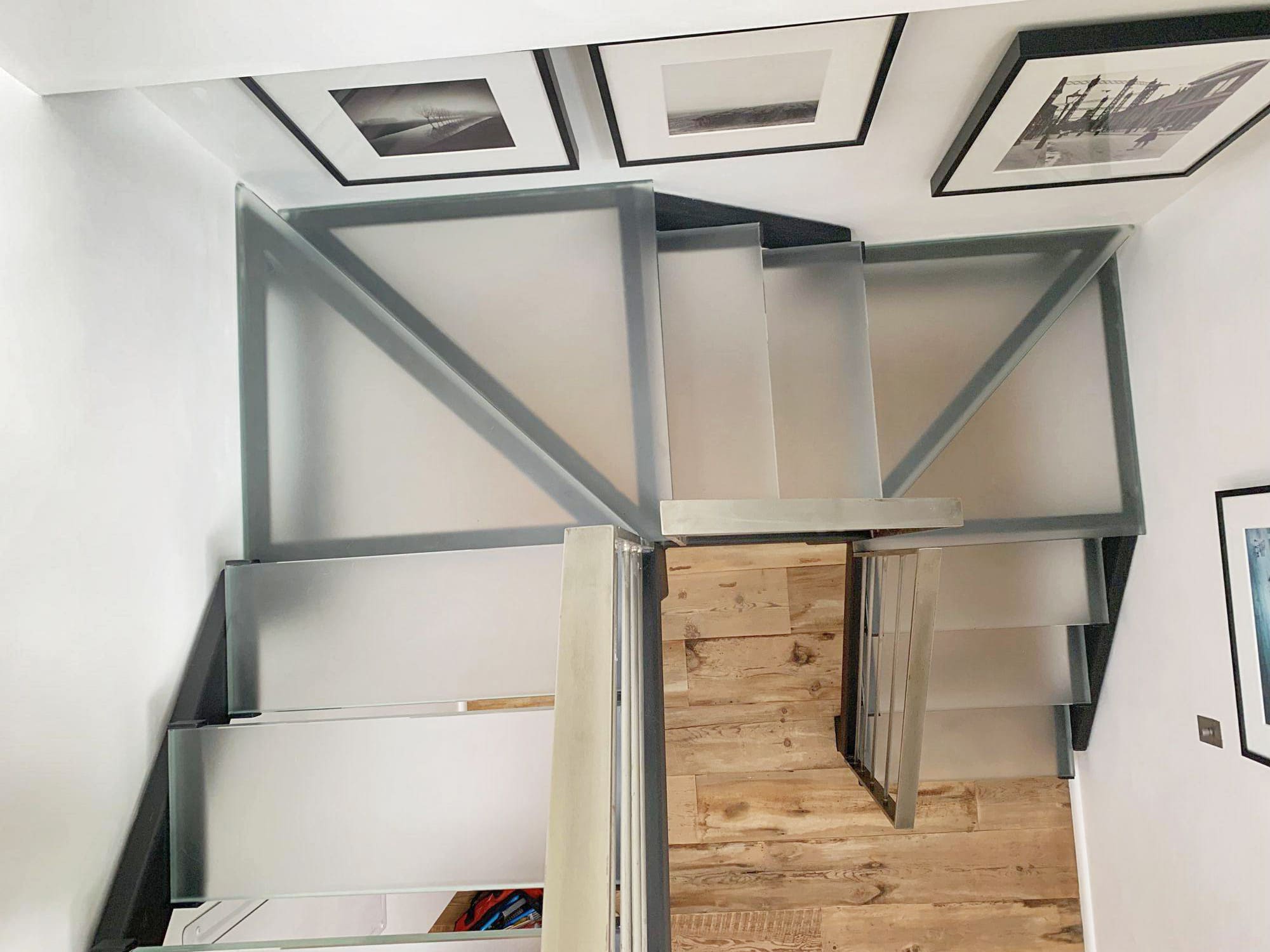 Interior residential staircase with glass side panels and wood steps viewed from above.