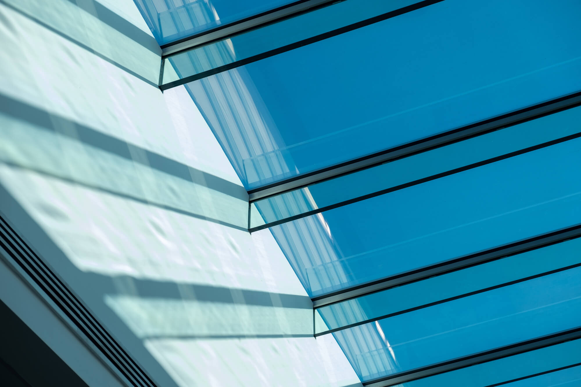 Close-up of stacked glass panels with sunlight passing through, highlighting reflections and clean linear edges.