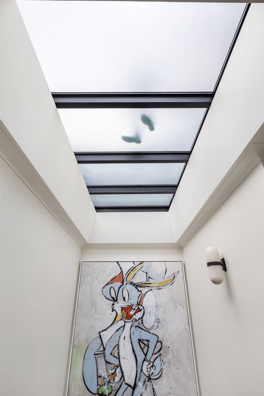Skylight window installed in a sloped roof above a hallway with modern art displayed.