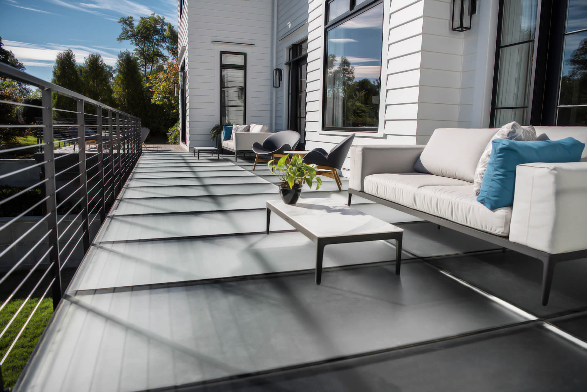 A modern home features a frosted glass patio floor with contemporary outdoor furniture and lush landscaping.
