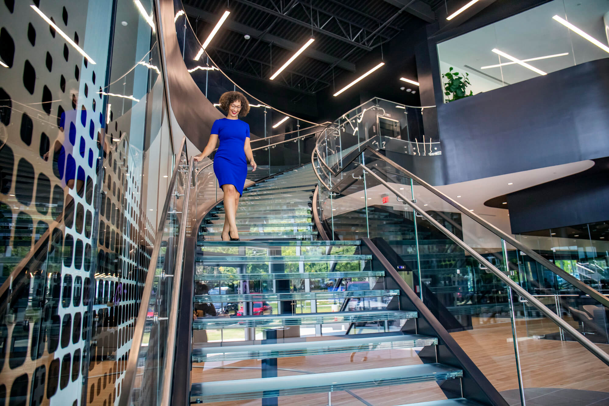 Person walking down a modern glass staircase with metal railings.