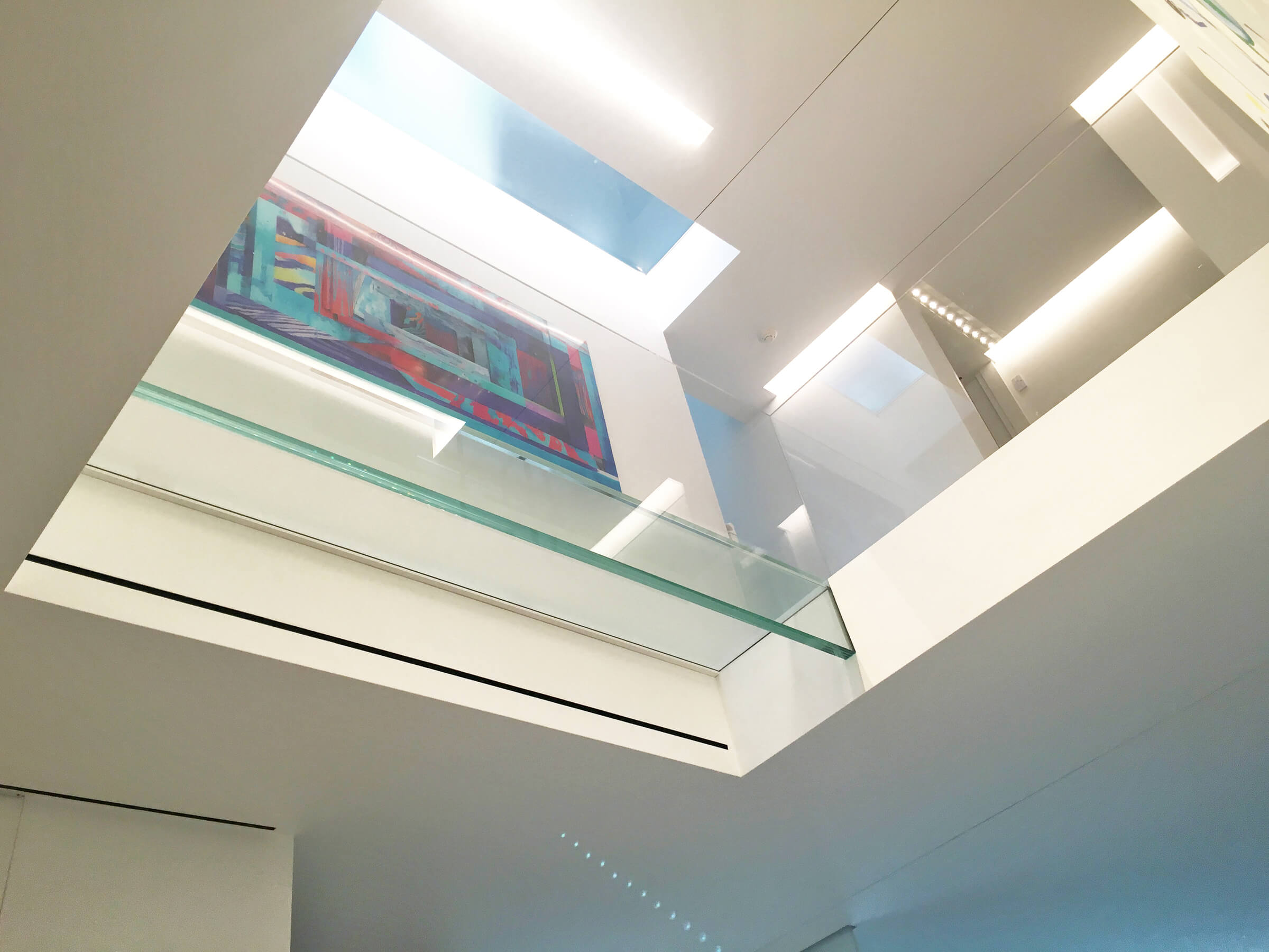 Interior of a contemporary home with large glass railings around an upper walkway under natural light.