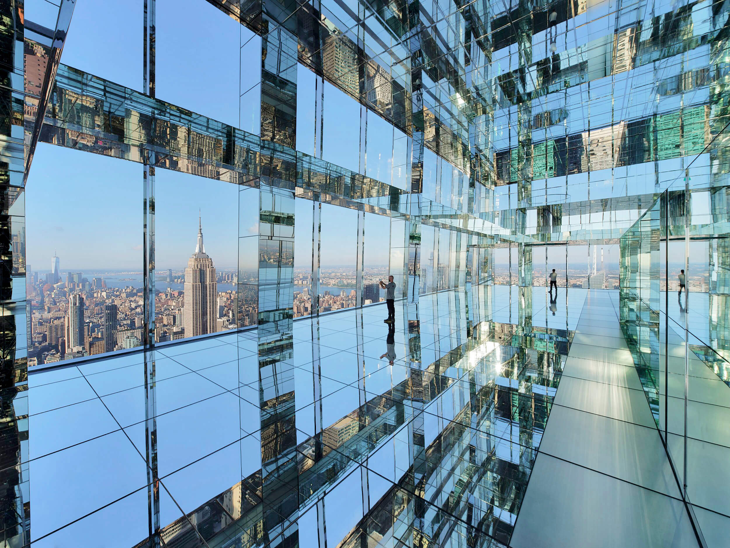 Glass observation deck with mirrored walls overlooking a skyline at sunset.
