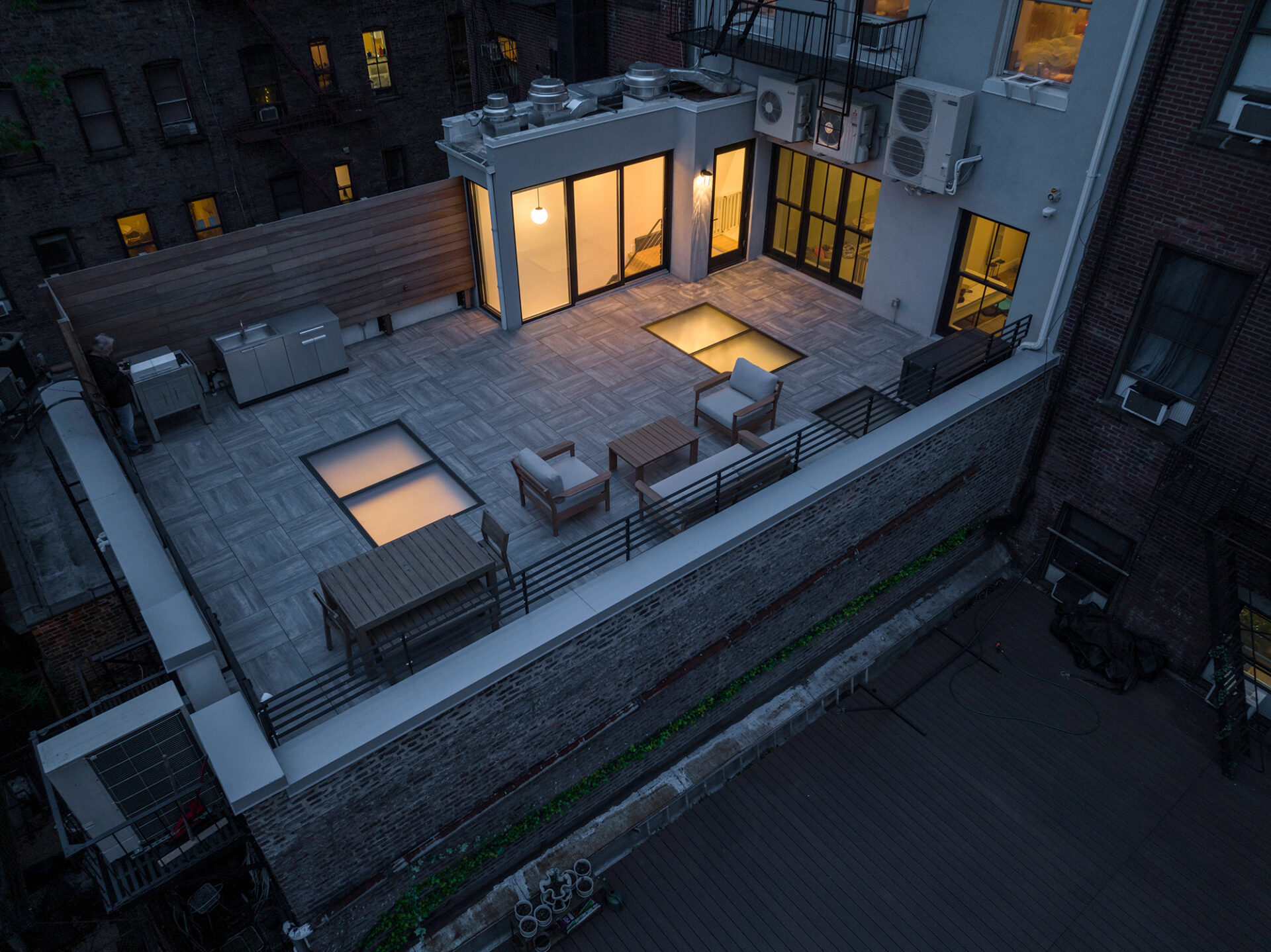 Aerial view of a rooftop deck with seating and glass floor panels at night.