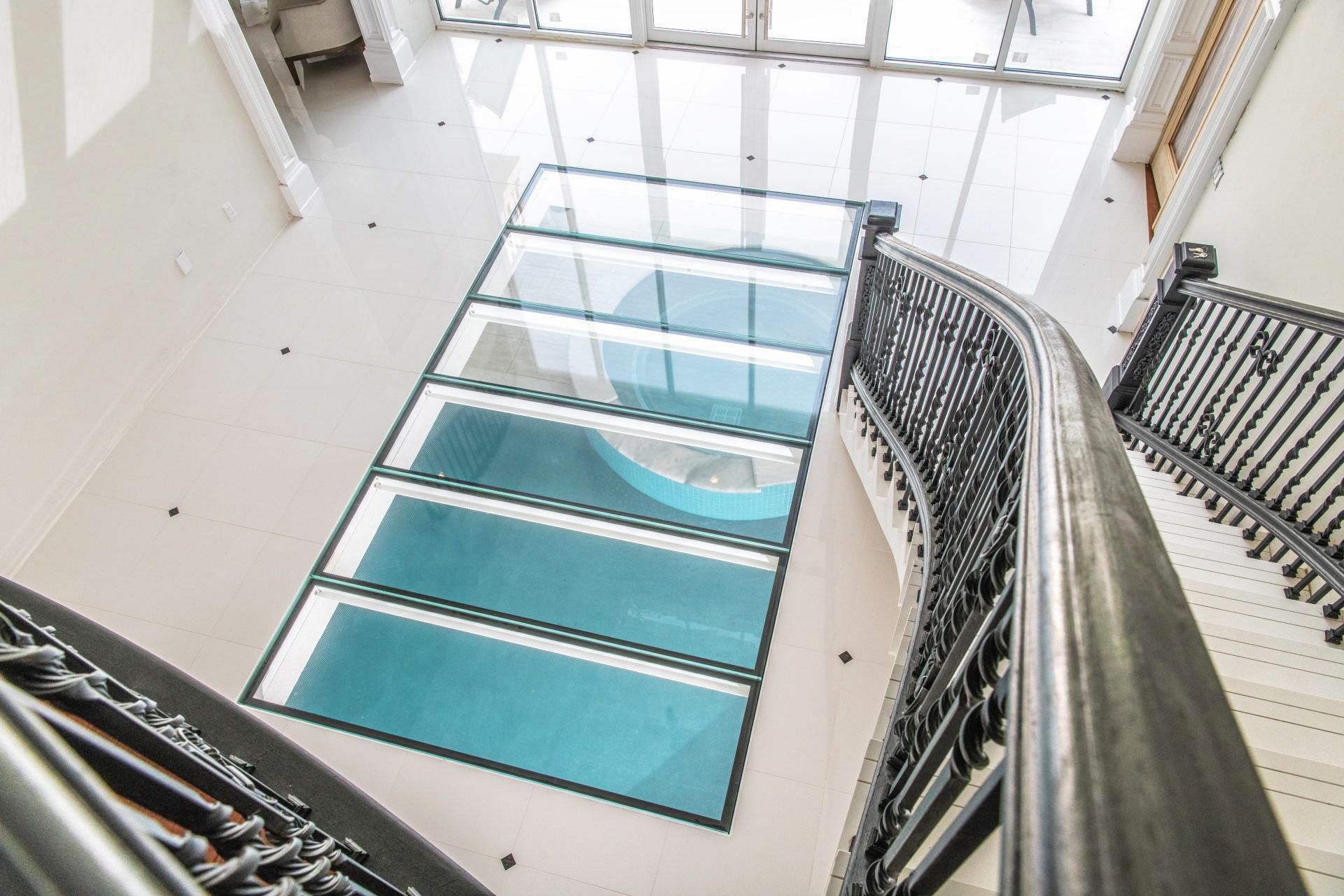 Staircase area with multiple glass floor panels installed in a row showing the pool beneath.
