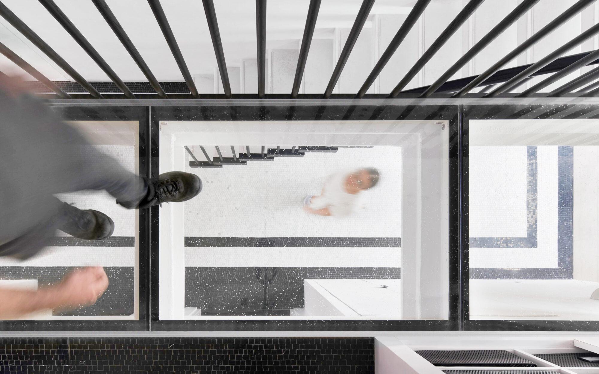 Top-down view of a glass floor panel with a person walking below.