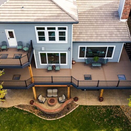 Drone view of a home with a large backyard deck featuring multiple glass floor panels and outdoor seating.