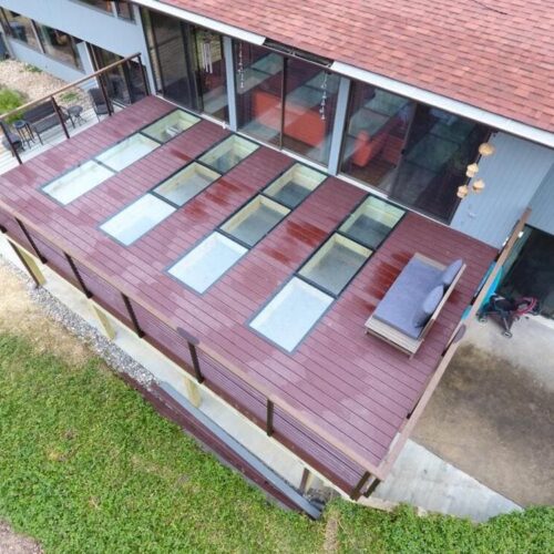 Angled aerial view of a long wooden deck with several rectangular glass floor panels and outdoor seating areas.