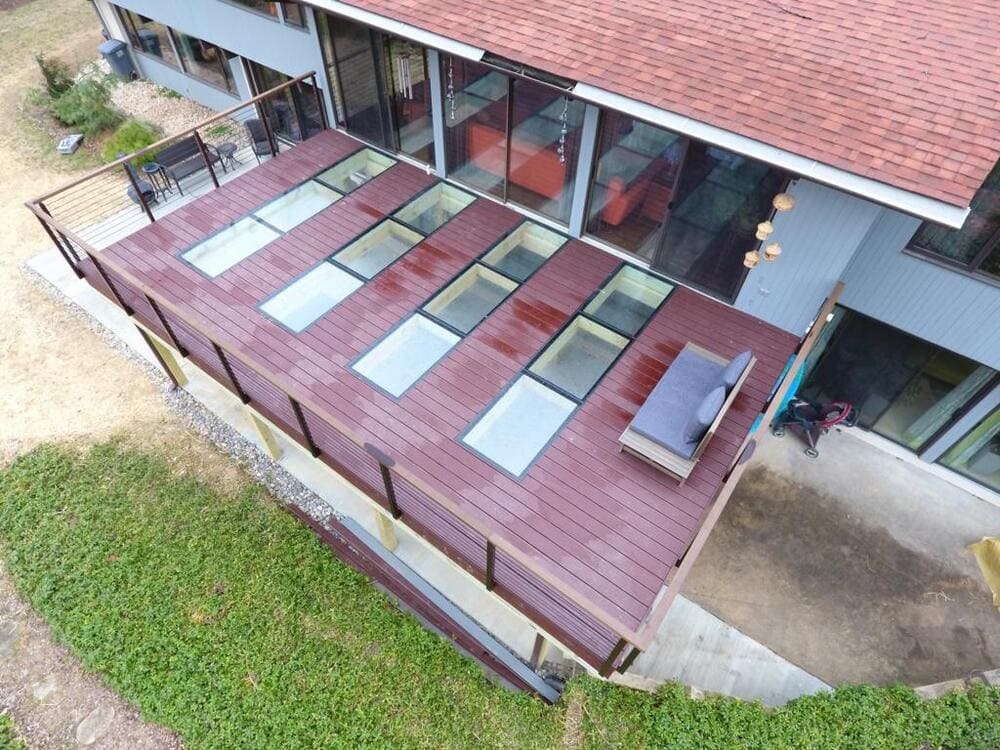 Angled aerial view of a long wooden deck with several rectangular glass floor panels and outdoor seating areas.