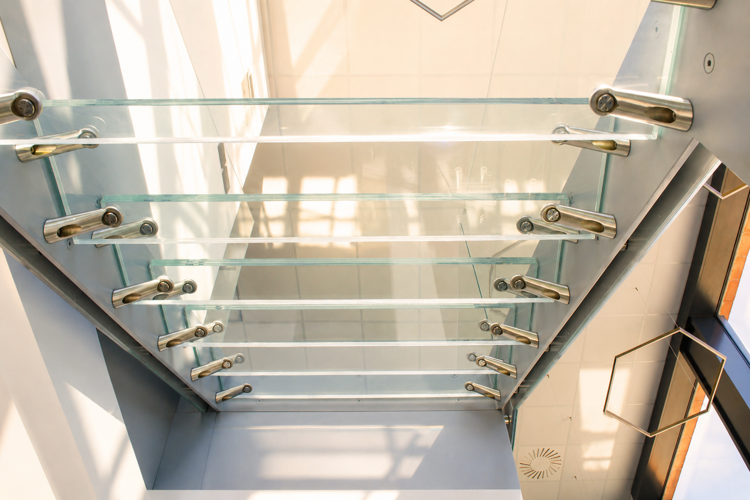 A view of a staircase from below with clear glass treads, glass railings and stainless steel hardware in a modern interior space.
