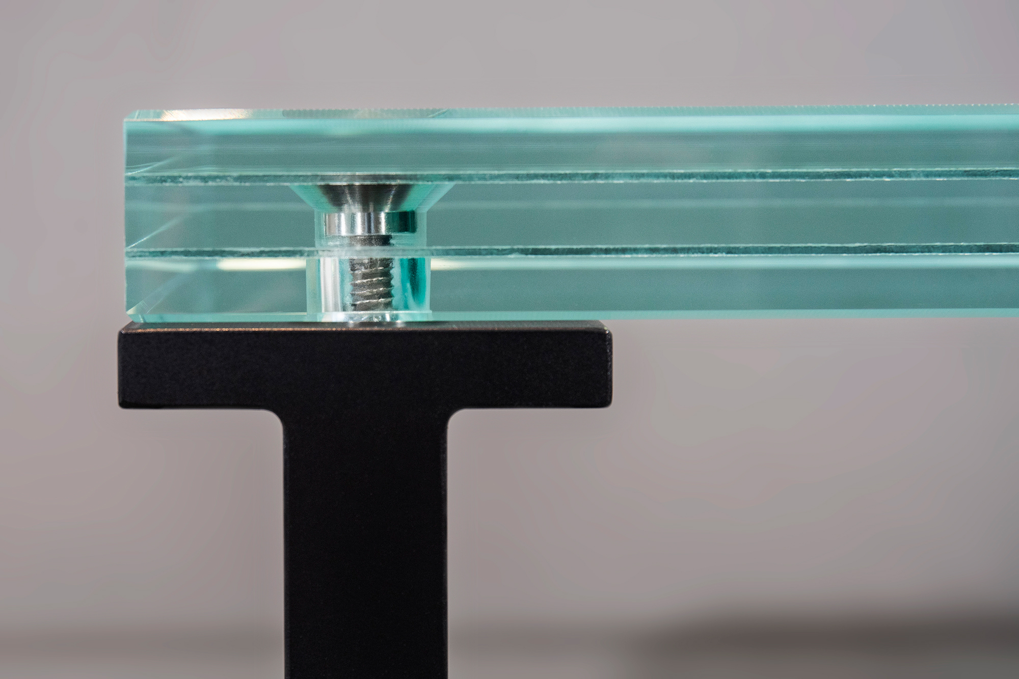 Close-up side view of a laminated glass stair tread with polished edges, a titanium embedded fastener, and a black aluminum support frame.