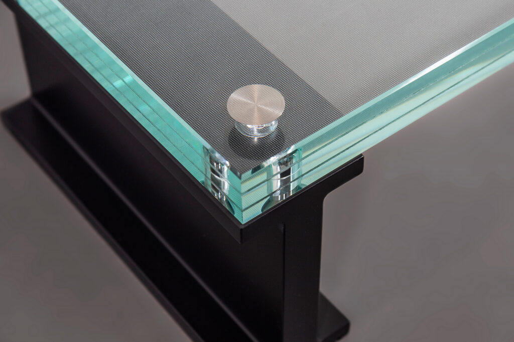 Close-up of a laminated textured glass stair tread with polished glass edges, titanium embedded fasteners, and a black aluminum support frame.