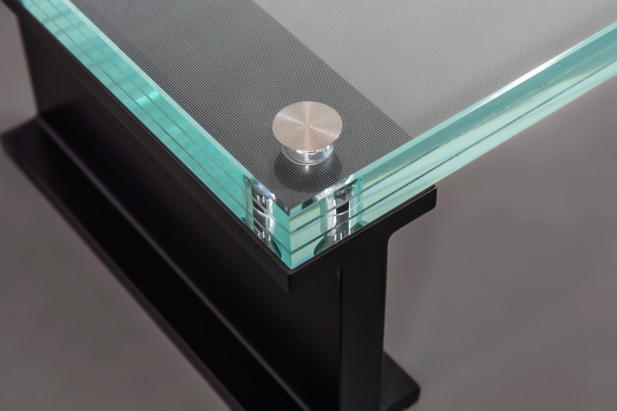 Close-up of a laminated textured glass stair tread with polished glass edges, titanium embedded fasteners, and a black aluminum support frame.