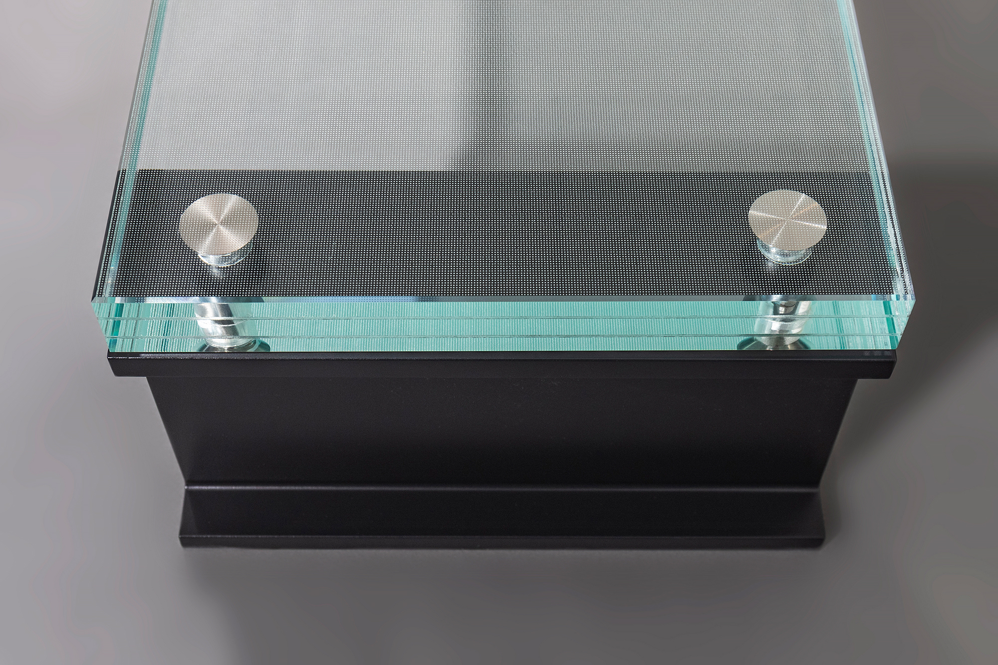 Close-up of a laminated glass stair tread with a NanoDot® anti-slip surface, polished edges, titanium embedded fasteners, and a black aluminum support frame.