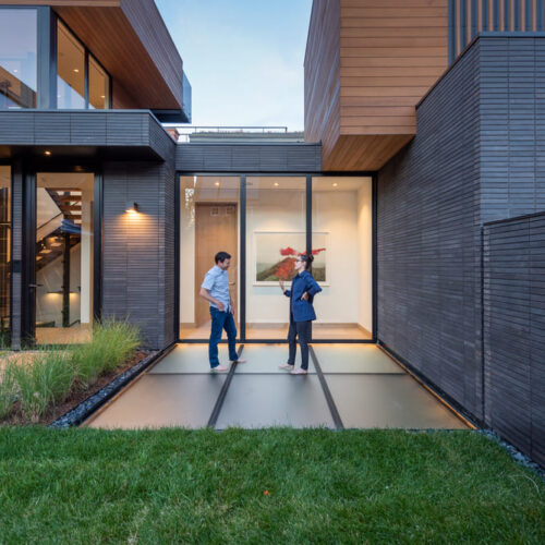 Modern house exterior with a glass skylight walkway beside a wooden structure.