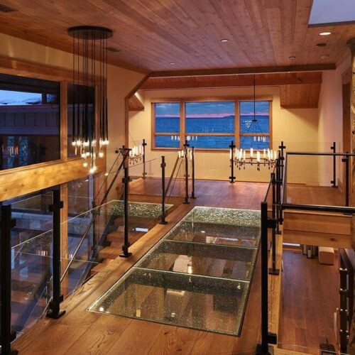 Rustic home interior with a suspended glass bridge floor and wooden railings.