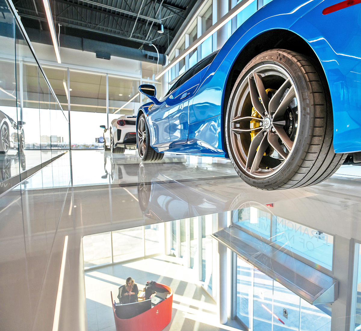 two luxury cars lined up, one in front of the other, on a drivable glass floor.