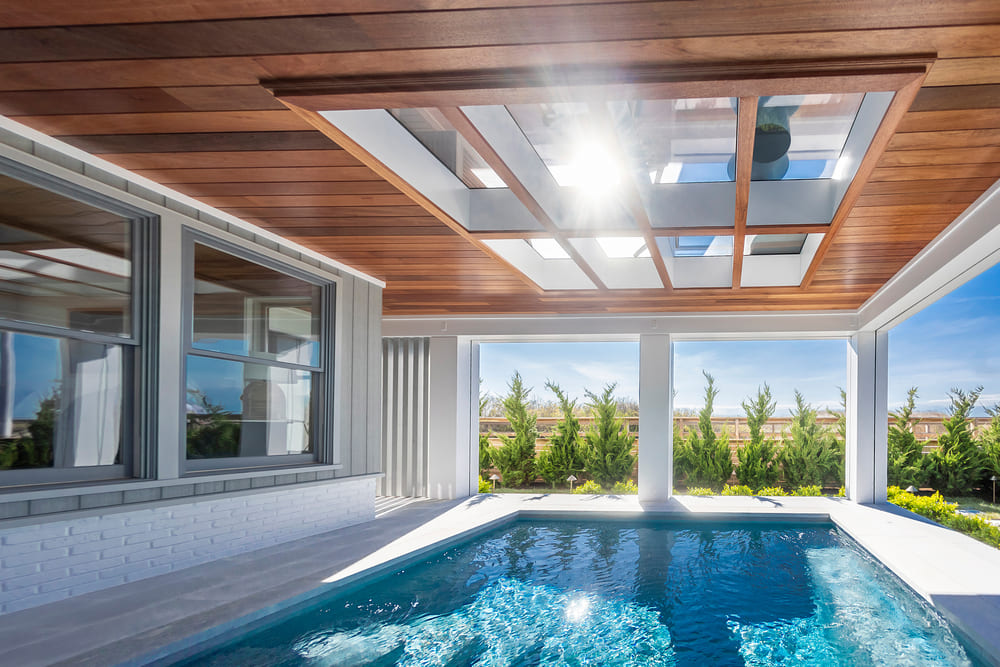 Indoor pool pavilion with glass walls, a wood-slat ceiling and a waterfront view