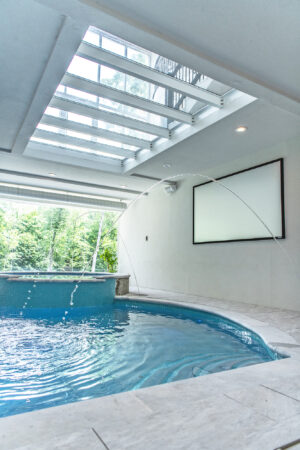 An indoor pool is illuminated by a large overhead glass skylight, blending luxury design with natural light.