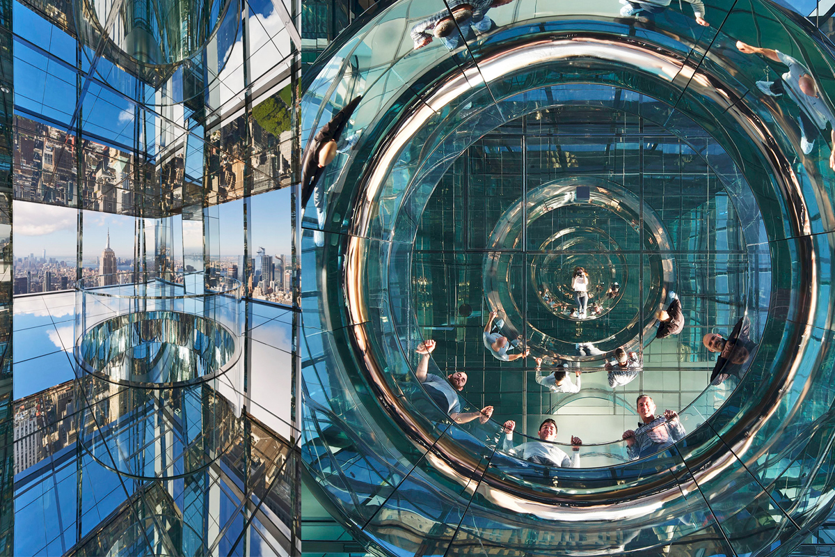 a shot from below, looking up at higher floors in a New York City skyscraper made mostly of glass, with smiling people looking down.