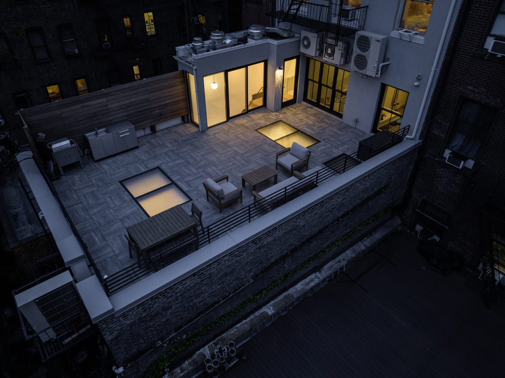 A rooftop terrace at night with outdoor seating and illuminated interior windows.