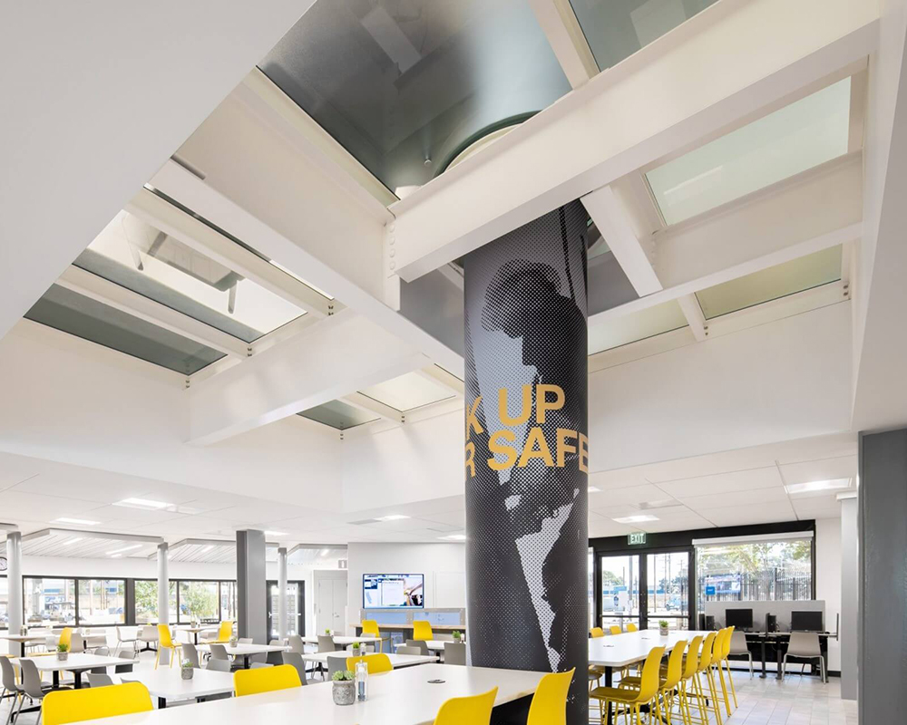 cafeteria space in a modern building with a glass ceiling and a striking central pillar