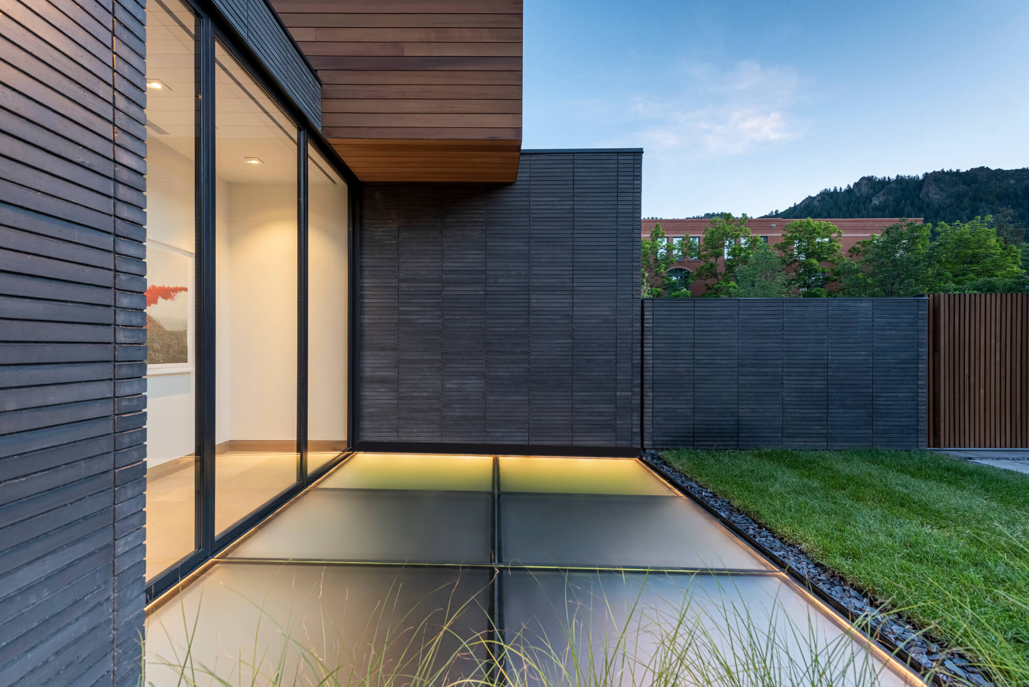 Flush walkable green roof skylight panels beside the exterior wall of a modern Aspen home at dusk, glowing from the living space below
