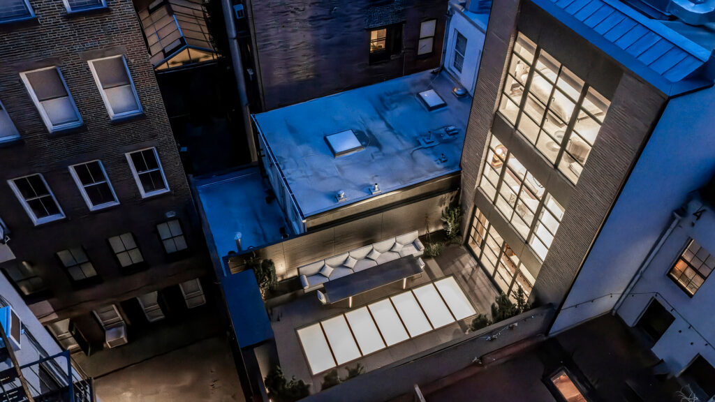 Aerial night view of a Greenwich Village townhouse rooftop terrace with an illuminated flush walkable glass skylight