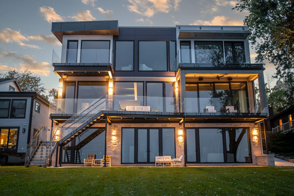 Modern lakefront home at dusk with an illuminated structural glass deck, glass balcony and exterior glass stairs by Glass Flooring Systems